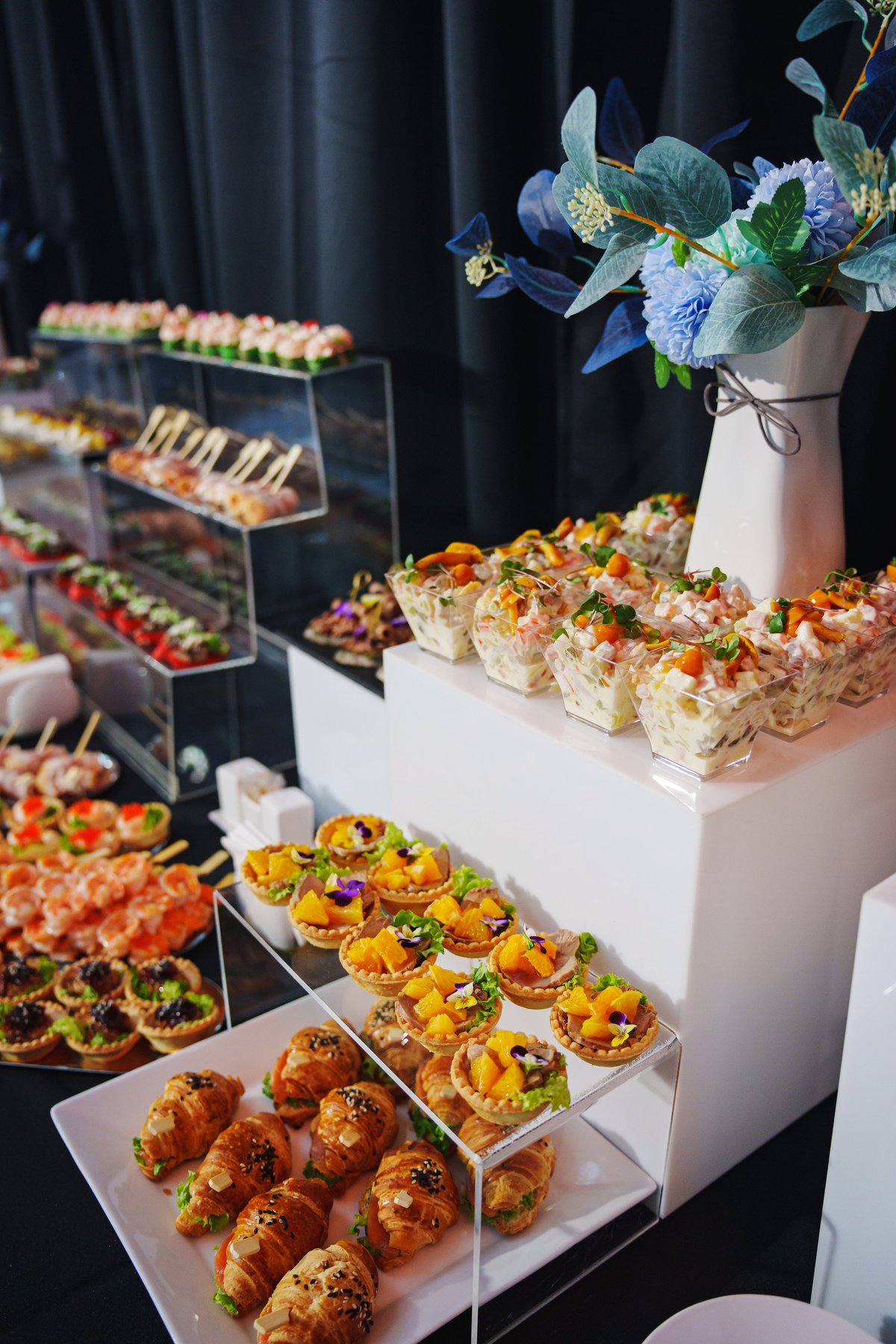 Elegant catered event display with tiered stands of gourmet canapés, tartlets and appetizers styled with a floral arrangement